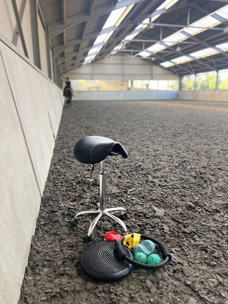 Op deze afbeelding zie je een zadelkruk in een bak staan, samen met diverse hulpmiddelen waar een fysio- of oefentherapeut gebruik van kan maken.